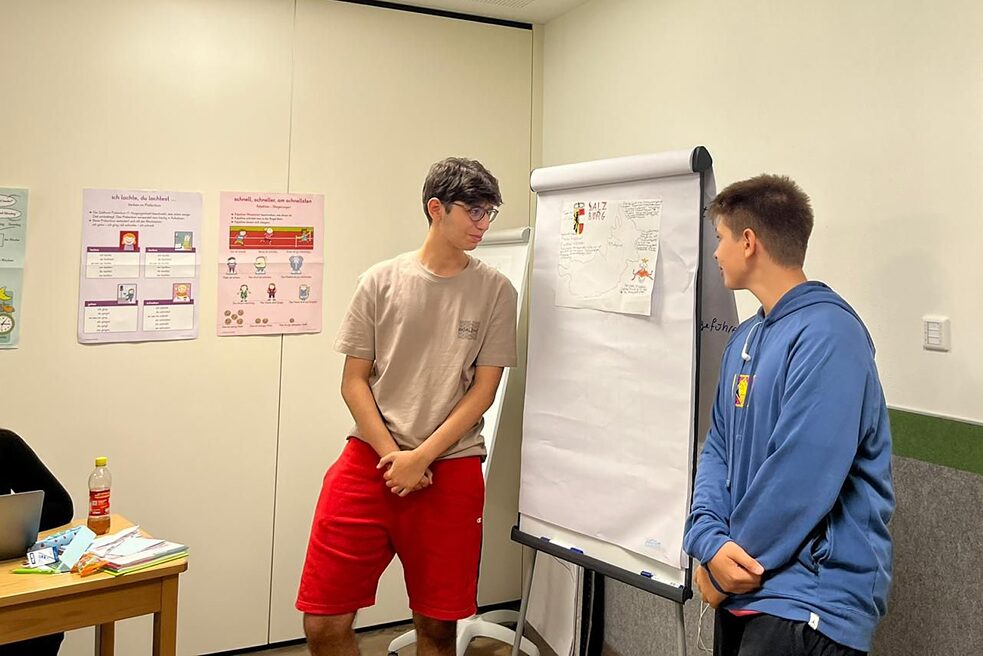 Jugendliche stehen an einer Pinnwant und referieren.