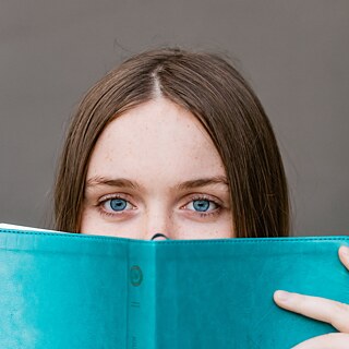 Ein Mädchen schaut über das Buch in die Kamera