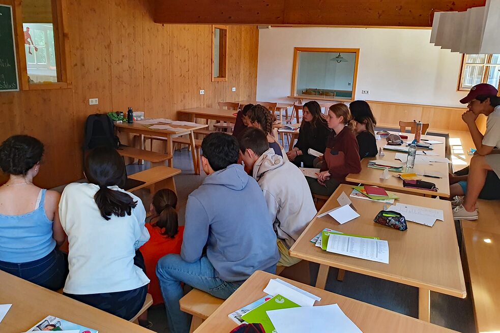 Jugendliche stitzen an Tischen und schreiben.