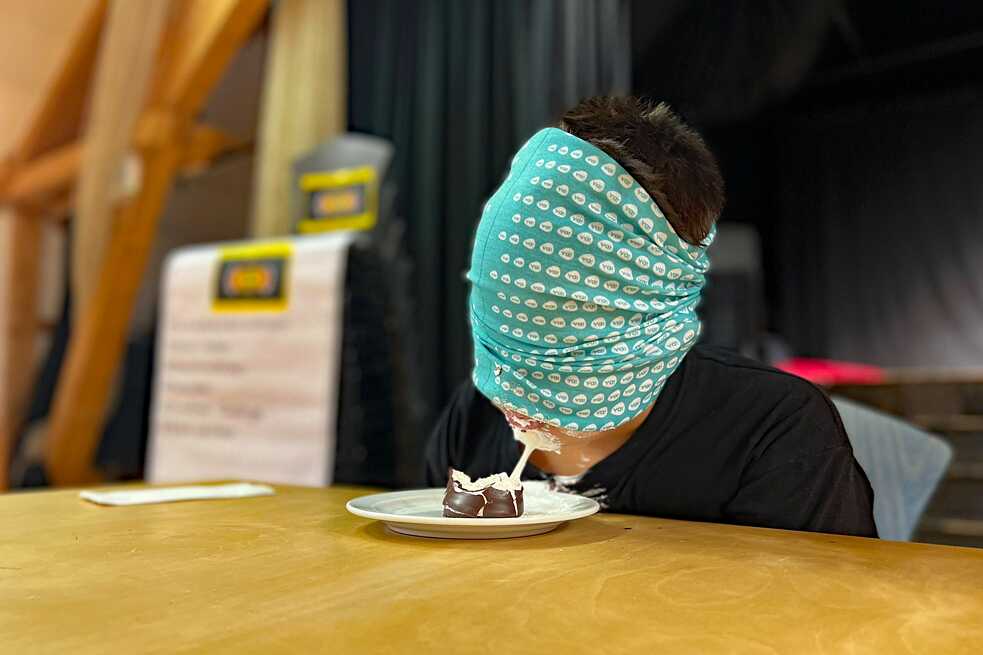 Jugendlicher mit verbundenen Augen isst eine Schwedenbombe.