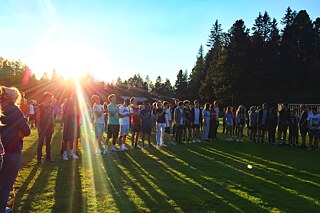 Jugendliche stehen auf einem Feld und blicken nach Oben. Im Hintergrund ein Wald und die Abendsonne.
