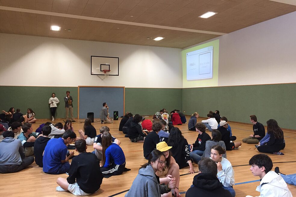 Jugendliche sitzen auf dem Boden einer Sporthalle.