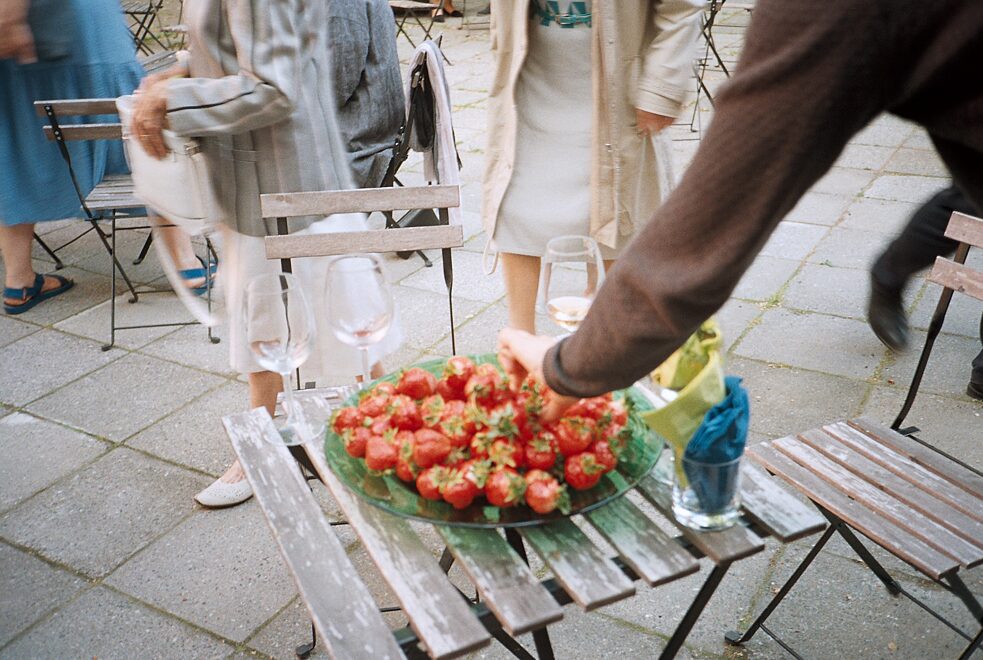 Человек берет ягоду клубники из большой миски на столе.