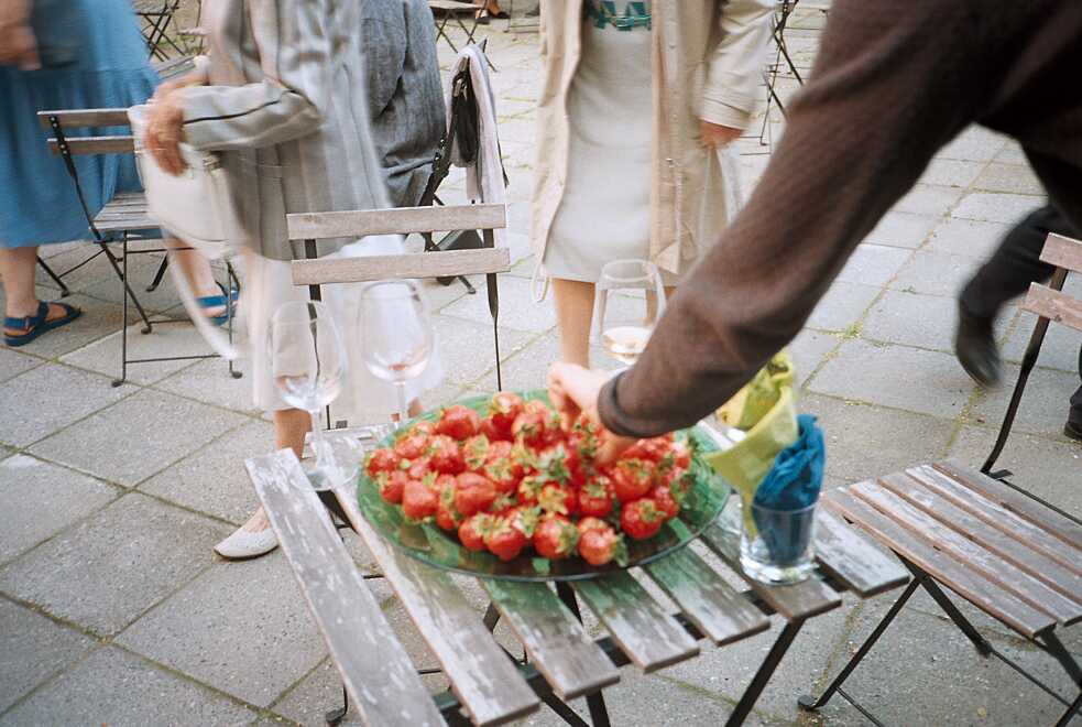 Eine Person greift nach einer der Erdbeeren, die in einer großen Schale auf einem Tisch stehen.