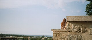 Eine Frau mit langen Haaren sitzt auf einer Mauer und genießt den Ausblick.