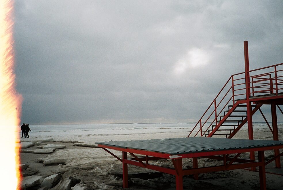 Красная конструкция у моря посреди зимнего пейзажа.
