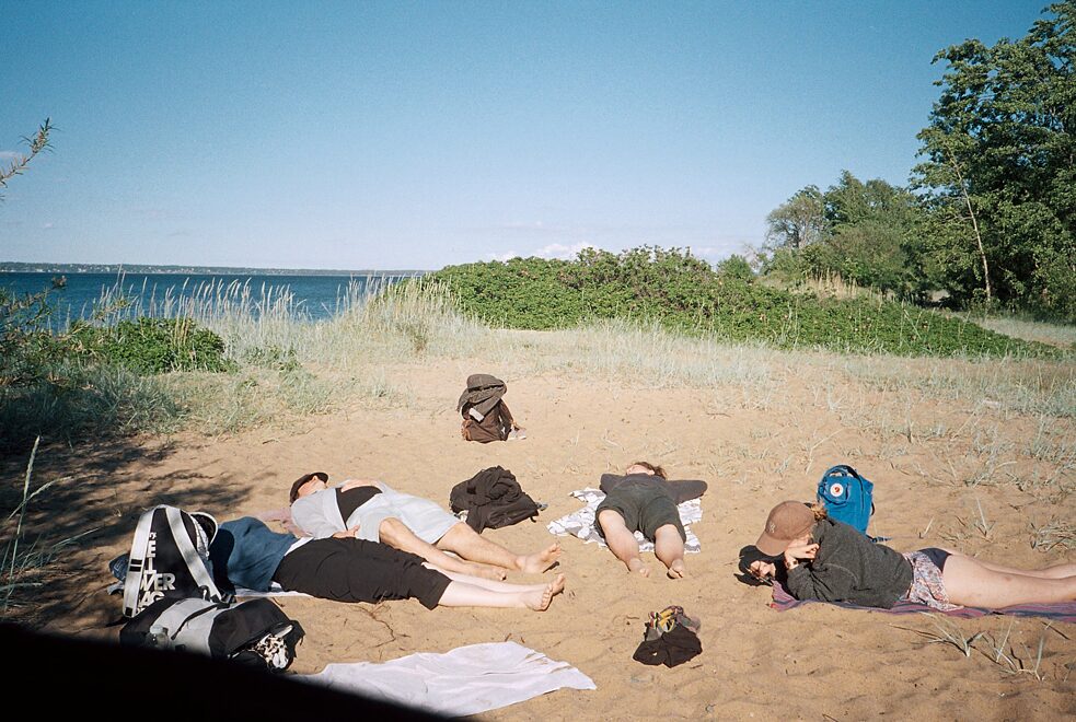 Vier Personen liegen im Kreis an einem Strand in der Sonne.