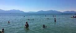 Menschen baden im Chiemsee, im Hintergrund die Berge.
