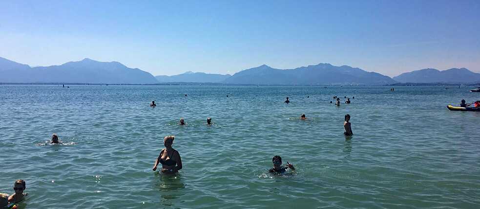 Menschen baden im Chiemsee, im Hintergrund die Berge.