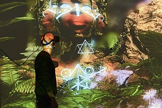 A visitor experiencing Alfredo Salazar-Caro’s VR artwork “Portrait of Elizabeth Mputu” during the exhibition “THE UNFRAMED WORLD” curated by Tina Sauerländer at the House of Electronic Arts in Basel, Switzerland, in 2017.