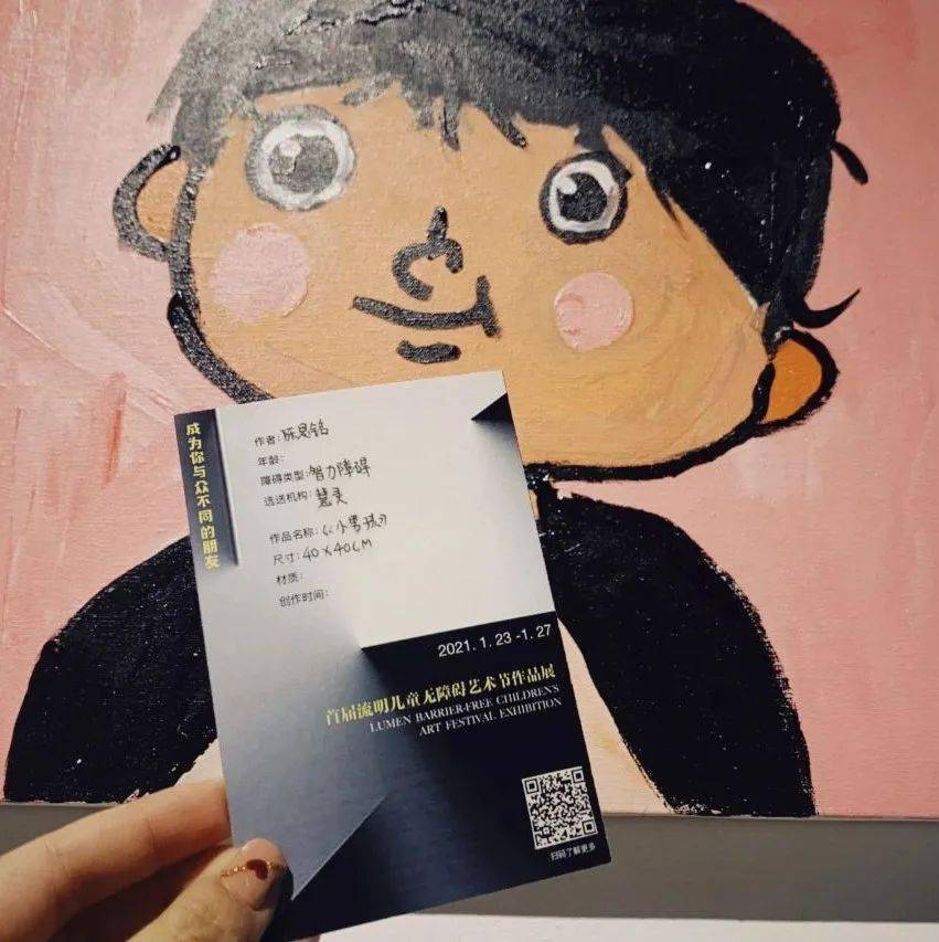 Photo of a hand holding an artwork label in front of a painting at Lumen Children’s Barrier-Free Art Festival