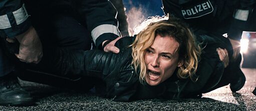 Eine blonde Frau wird von zwei Polizisten auf den Boden gedrückt.