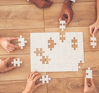 Aufnahme von oben auf einen Tisch. Mehrere Personen setzen ein Puzzle zusammen.