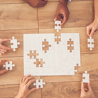 Aufnahme von oben auf einen Tisch. Mehrere Personen setzen ein Puzzle zusammen.