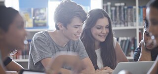 Mehrere Schüler arbeiten mit Tablets und Laptop in der Bibliothek.