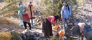 امرأة وأطفال ورجل في منطقة جافة يملؤون زجاجاتهم من أحد الآبار.