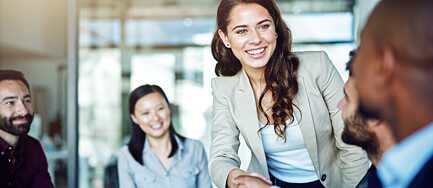 Eine Gruppe junger Geschäftsleute in einem Sitzungsraum; eine junge Frau reicht einem Mann die Hand.