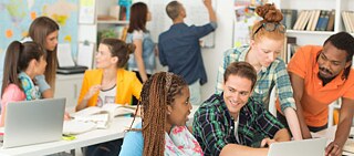 alunos discutem em sala de aula, em dois grupos diferentes, em duas mesas, em imagem representando o alemão das escolas públicas