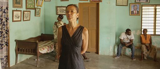 Foto eines Wartezimmers. Einige Menschen sitzen auf einer Bank. Eine stehende Frau im Vordergrund. Alle scheinen afrikanisch zu sein.