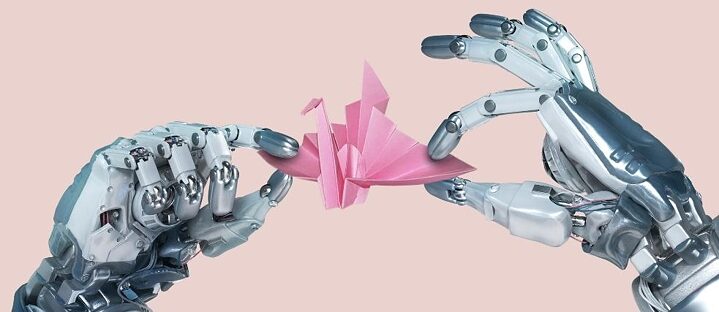 Two robotic hands hold an origami crane. The background is pink and offers space for editorial text.