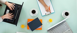 Die Kursteilnehmer bei der Gruppenarbeit. Sie schreiben ihre Notizen auf Schreibblöcke und an Laptops. Blick von oben.