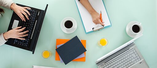 Die Kursteilnehmer bei der Gruppenarbeit. Sie schreiben ihre Notizen auf Schreibblöcke und an Laptops. Blick von oben.
