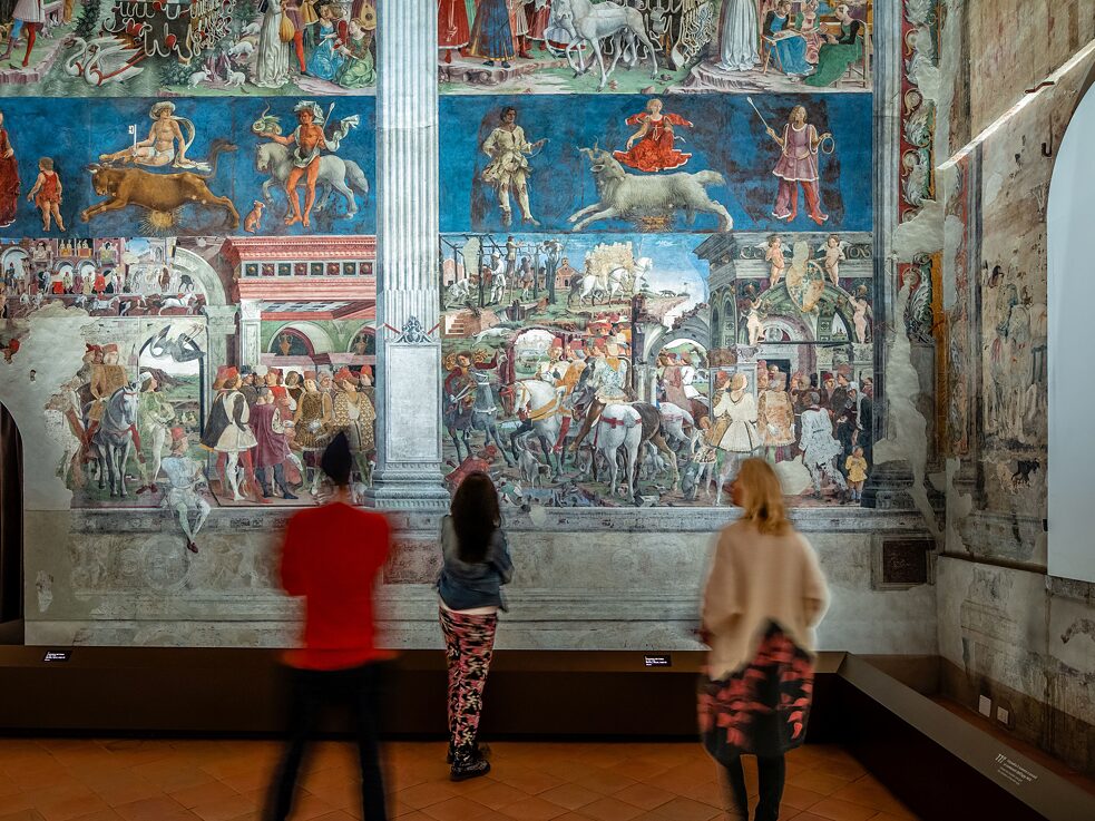 Drei Menschen, die die Wandgemälde im Museum Palazzo Schifanoia betrachten .