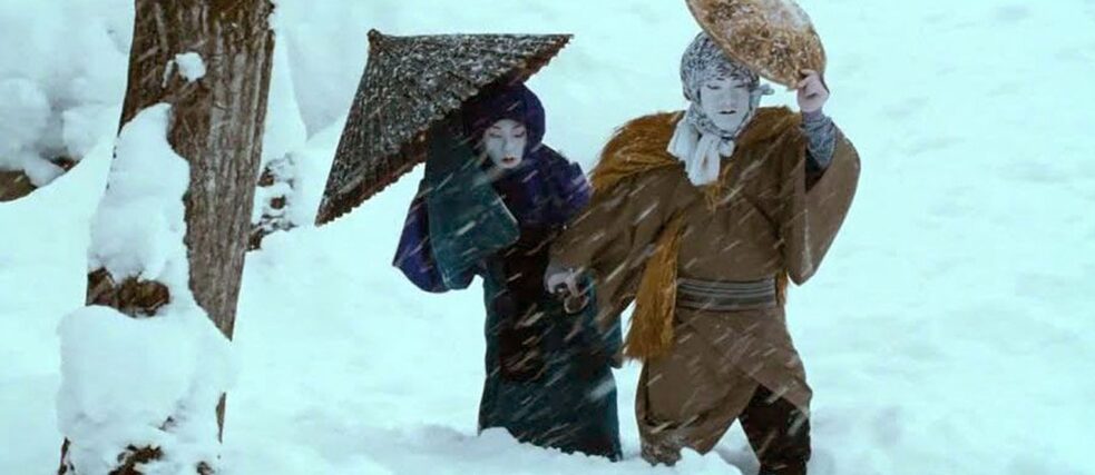 Zwei Personen in auffälligen Kostümen laufen durch hohen Schnee. 