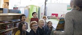 Pohled zezadu na učitelku, která čte knihu dětem předškolního věku. Děti se smějí a jsou šťastné.