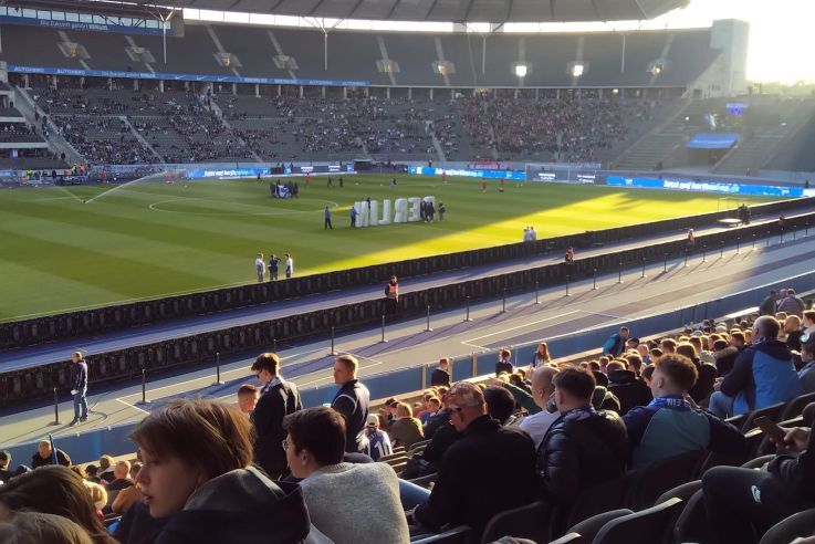 Ein großes Stadion aus Publikumsperspektive, vor dem Spiel, auf dem Rasen steht ein "Berlin"-Aufsteller
