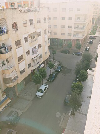Hallo, Ich wohne in dieser Nachbarschaft, es ist ruhig heute, aus meinem Fenster sehe ich einige Autos und Häuser, manchmal spielen Kinder, und auch einige Schüler, die auf dem Weg zur Schule sind, kommen hier vorbei