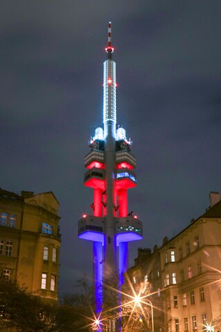 Auf dem Foto ist der Fernsehturm Žižkov bei Nacht zu sehen. Er ist in den Farben der tschechischen Flagge angestrahlt.