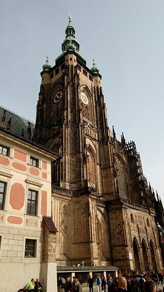 Auf dem Foto ist die Prager Burg zu sehen. In der Mitte des Bildes ragt der Kirchturm in die Höhe, im Hintergrund ist blauer Himmel zu sehen.