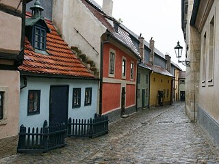 Auf dem Foto ist das Goldene Gässchen Prags zu sehen. Man sieht viele kleine Häuser in blau, rot, grün und gelb bei bewölktem Himmel.