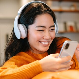 Eine junge Frau mit Kopfhörern wählt einen Podcast am Handy aus