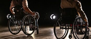 Vista desde el escenario con dos actores en silla de ruedas orientados hacia el público