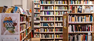 Vier Regale sind mit Büchern gefüllt. Auf den Regalen links vorne und rechts stehen vereinzelt Bücher und Infozettel.