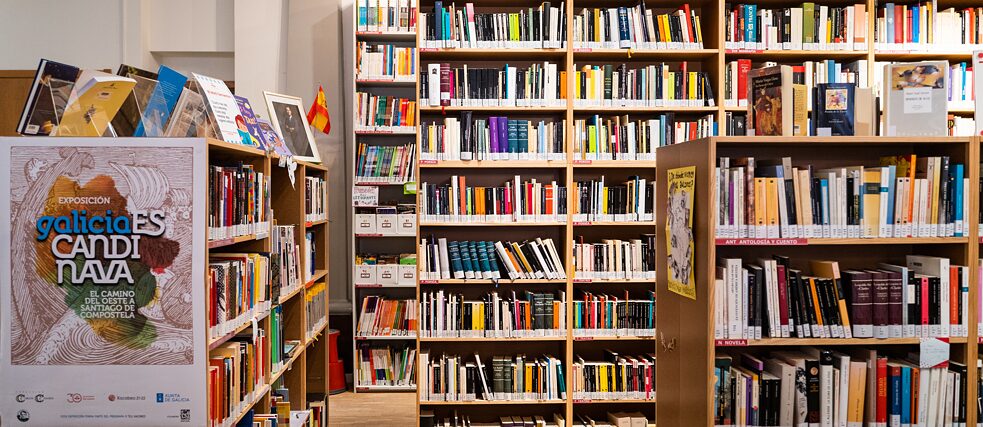 Vier Regale sind mit Büchern gefüllt. Auf den Regalen links vorne und rechts stehen vereinzelt Bücher und Infozettel.