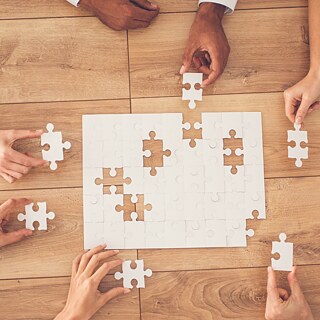 Aufnahme von oben auf einen Tisch. Mehrere Personen setzen ein Puzzle zusammen.