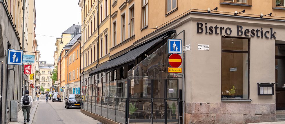 Außenansicht von einer Straßenecke. Das Haus im Vordergrund hat einen bestuhlten Wintergarten.