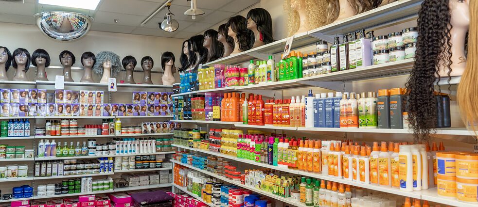 Verkaufsregale gefüllt mit unterschiedlichen bunten Haarpflegeprodukten. Auf dem obersten Regalbrett stehen mehrere Perücken auf Ständern.