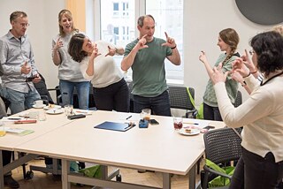 Eine Gruppe von Lehrkräften steht um einen Tisch und macht Fotogesten.