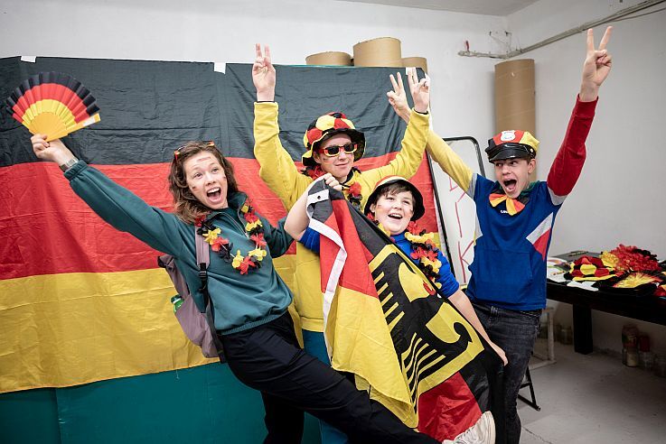 Eine Gruppe posiert lachend vor einer Deutschlandflagge.