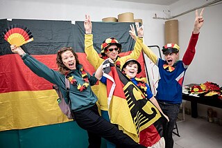 Eine Gruppe posiert lachend vor einer Deutschlandflagge.