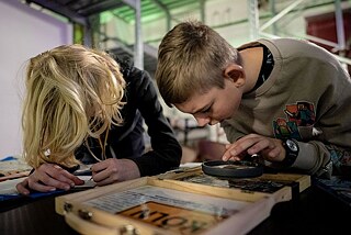 Zwei Jungen beugen sich über ein Spiel und schauen durch eine Lupe.