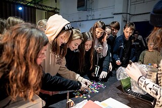 Kinder stehen um einen Tisch und suchen sich bunte Ansteckbuttons aus.