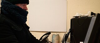 Ein Mann mit Mütze und Schal arbeitet am Schreibtisch