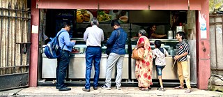 Six people stand in line outside the snack bar waiting for their food