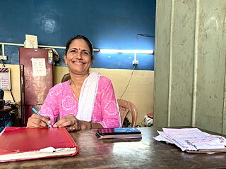 A woman (Sauli) sits at a desk and smiles at the camera