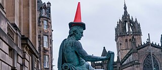 Statue eines Philosophen mit rotem Verkehrskegel auf dem Kopf